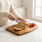 person-slicing-bread-on-blank-wooden-board-with-tomatoes